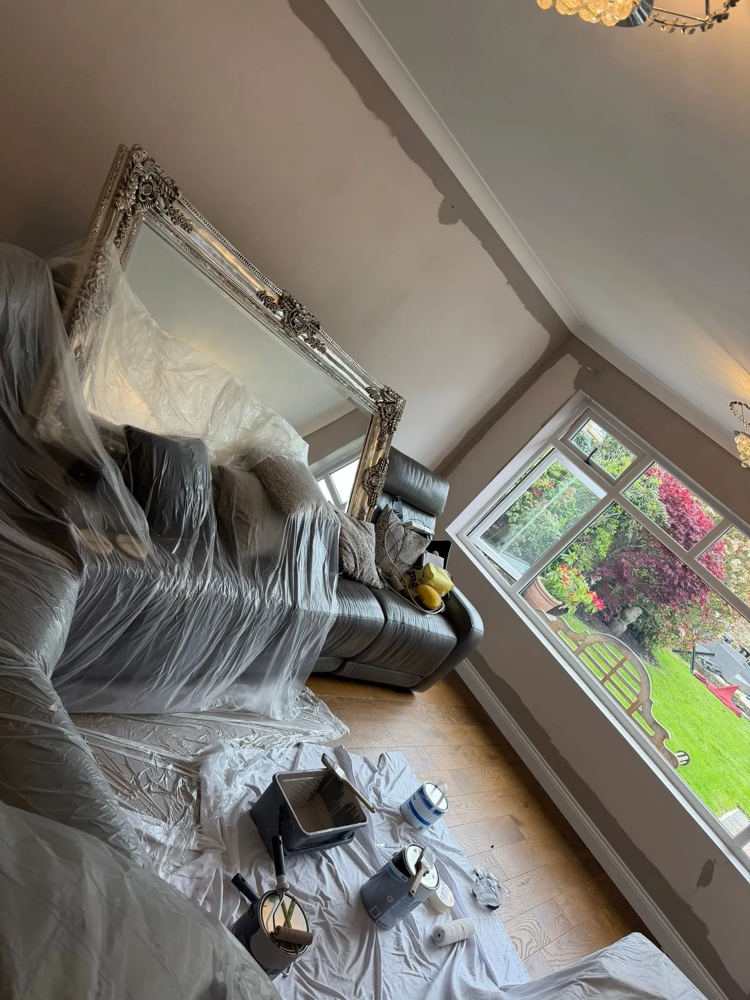 Living room with sofas, a large mirror and the floor covered in dust sheets ready for painting